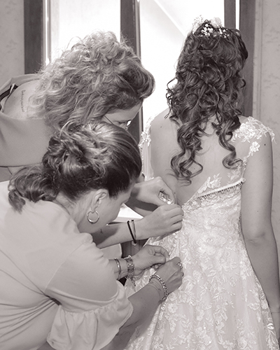 Immagine della mamma che sistema il vestito alla futura sposa, foto scattata in studio da Ferruccio Munzittu